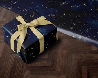 May include: A navy blue gift box with a gold ribbon and a constellation pattern. The box is sitting on a dark wood floor.