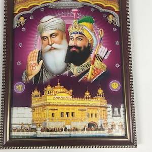 May include: A framed print of a religious image featuring two Sikh gurus, Guru Nanak and Guru Gobind Singh, with the Golden Temple in the background. The image is set against a purple background with gold accents.