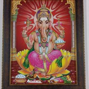 May include: A framed print of the Hindu deity Ganesha, depicted with an elephant head and multiple arms. Ganesha is seated on a lotus flower, wearing colorful garments and jewelry. The background is a vibrant red with gold accents.