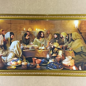 Op de afbeelding: Een ingelijste prent die het Laatste Avondmaal uitbeeldt. Het kunstwerk toont een tafel met eten en drinken, omringd door figuren in gewaden. De scène wordt verlicht door kaarsen en fakkels, met een goudkleurige, sierlijke lijst.