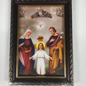 May include: A framed religious print depicting the Holy Family. The image shows Mary, Joseph, and Jesus standing together. The background features a dove and a cross. The frame is brown with gold accents.