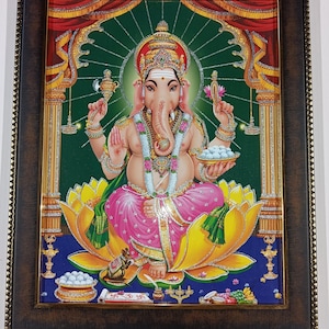 May include: A framed, colorful image of the Hindu deity Ganesha, seated on a lotus flower. Ganesha is depicted with an elephant head, adorned with jewelry, and holding various items. The artwork features vibrant colors and intricate details, set against a green and red backdrop.