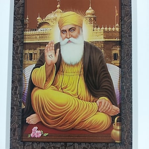 May include: A rectangular framed print featuring a portrait of Guru Nanak Dev Ji with a long white beard, wearing a yellow turban and robe with a dark shawl. The figure sits before a golden temple, with a hand raised showing the Ik Onkar symbol.