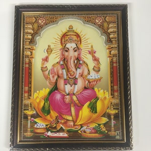 May include: Framed artwork depicting the Hindu deity Ganesha, seated on a lotus flower. The image features vibrant colors, including pink, gold, and yellow, with intricate details and ornate embellishments. The frame is dark brown with a decorative border.