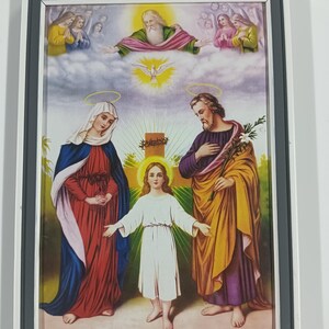 Puede incluir: Obra de arte religiosa enmarcada que representa a una familia con halos, una cruz y figuras en las nubes. La obra utiliza rojo, azul, amarillo y blanco. El marco es gris y blanco.