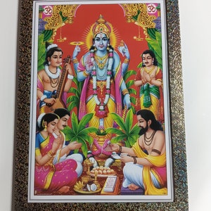 May include: A framed religious print depicting a Hindu deity, Vishnu, in a colorful, ornate setting. The deity is surrounded by other figures, including a couple performing a ritual. The print is framed in a brown frame with a gold-colored design.