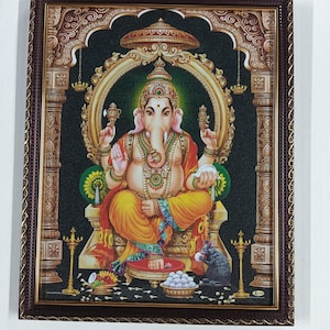 May include: A framed print of the Hindu deity Ganesha, depicted in vibrant colors. Ganesha is seated on a throne, adorned with jewelry, and surrounded by ornate details. The frame is a dark brown color.