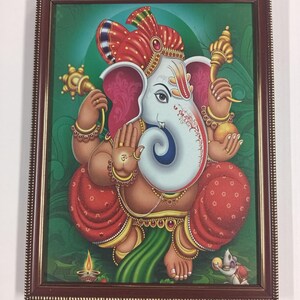 May include: A framed print of the Hindu deity Ganesha, depicted with a white elephant head, adorned in red and gold garments, and holding various symbolic objects. The background is a gradient of green, and the frame is brown.