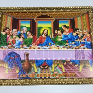 Op de afbeelding: Een ingelijst schilderij dat het Laatste Avondmaal voorstelt, een christelijk religieus tafereel. Jezus Christus zit in het midden van een tafel met zijn discipelen. Het schilderij is geschilderd tegen de achtergrond van een kamer met een houten plafond en ramen. Het schilderij is ingelijst in een gouden lijst met sierlijke details. De tekst "I AM THE BREAD OF THE LIFE" staat onderaan het schilderij.