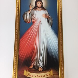 May include: A framed religious print showing a figure in white and red robes, with a golden halo and an outstretched hand. The image has a blue background and the text "Jesus, I trust in You" on a banner. The frame is gold.