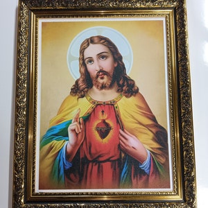 May include: A framed religious print depicting Jesus Christ with a golden halo and a red heart with thorns on his chest. The frame is ornate and gold.