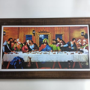 Op de afbeelding: Een ingelijst schilderij dat het Laatste Avondmaal voorstelt, een beroemde Bijbelse scène. Het schilderij toont Jezus Christus en zijn discipelen die rond een tafel zijn verzameld, met een houten achtergrond en een warm kleurenpalet.