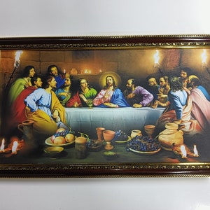 Op de afbeelding: Een ingelijst schilderij dat het Laatste Avondmaal voorstelt, een bijbelse scène waarin Jezus een maaltijd deelt met zijn discipelen. Het schilderij toont een groep mannen die rond een tafel zitten, met Jezus in het midden. Het schilderij speelt zich af in een zwak verlichte kamer, met kaarsen die de scène verlichten. Het schilderij is ingelijst in een donkerhouten lijst met gouden accenten.