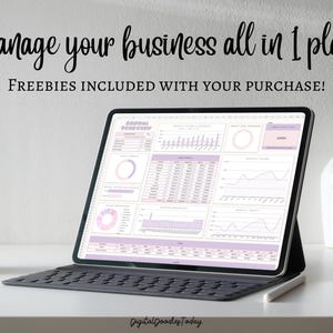 May include: A laptop computer displaying a spreadsheet with charts and graphs in shades of pink and purple. The text "Manage your business all in 1 place" and "FREEBIES INCLUDED WITH YOUR PURCHASE!" is displayed at the top of the screen. The laptop is on a white desk with a white mug and a white vase.