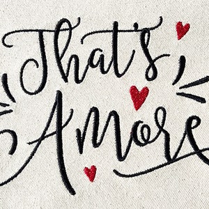 May include: Black and white embroidered design on a white canvas background. The design says "That's Amore" with red hearts scattered around the text.