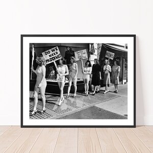 K&ouml;nnte beinhalten: Schwarzwei&szlig;foto einer Gruppe von Frauen, die Schilder mit den Aufschriften "Do We Need Padding?" und "United We Stand Divided We Fall" halten. Die Frauen tragen Badeanz&uuml;ge und stehen auf einer Stra&szlig;e in der Stadt.