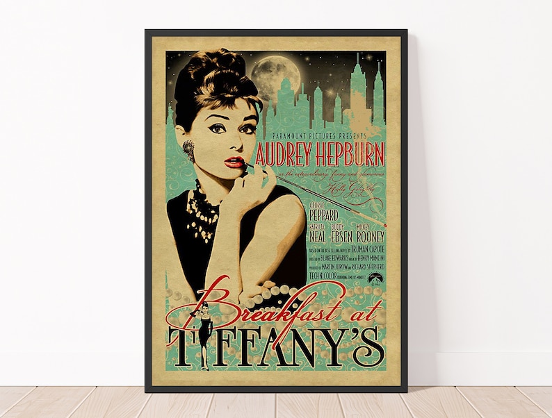 May include: A framed vintage movie poster for "Breakfast at Tiffany's" featuring Audrey Hepburn. The poster has a teal and beige background with the title in a stylized font. The image includes a silhouette of a city skyline and a full moon.