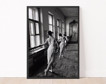 May include: Black and white photograph of a ballet studio with five ballerinas in white tutus practicing in front of a large mirror. The ballerinas are facing the mirror and are in various positions.
