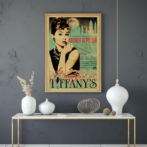 May include: A framed vintage movie poster for "Breakfast at Tiffany's" featuring Audrey Hepburn. The poster has a gold frame and a teal and beige color scheme. The title and Hepburn's name are prominently displayed.