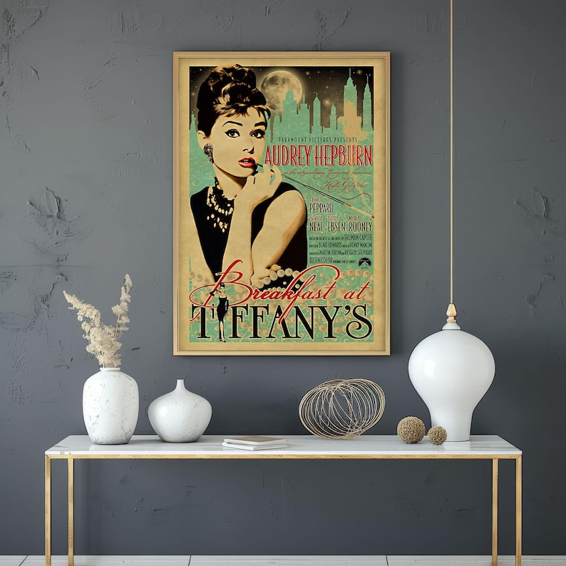 May include: A framed vintage movie poster for "Breakfast at Tiffany's" featuring Audrey Hepburn. The poster has a gold frame and a teal and beige color scheme. The title and Hepburn's name are prominently displayed.