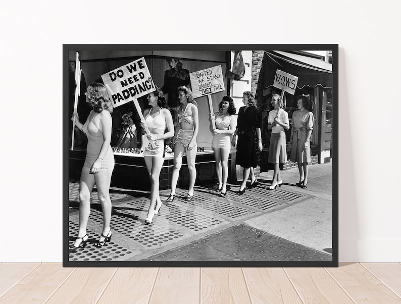 K&ouml;nnte beinhalten: Schwarzwei&szlig;foto einer Gruppe von Frauen, die Schilder mit den Aufschriften "Do We Need Padding?", "United We Stand Divided We Fall" und "Wows" halten. Die Frauen tragen Badeanz&uuml;ge und stehen auf einem B&uuml;rgersteig.