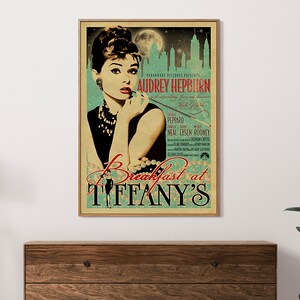 May include: A framed vintage movie poster for "Breakfast at Tiffany's" featuring Audrey Hepburn. The poster has a teal and beige color scheme with the film's title and credits. The image is displayed on a wooden dresser.