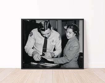 May include: A black and white historical photograph showing a police officer in a uniform and tie taking fingerprints from a woman wearing glasses and a collared jacket. The officer is looking down at the woman's hand while she stands beside him.