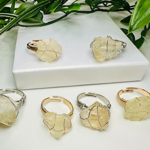 Puede incluir: Cinco anillos con piedras de diferentes colores envueltos en alambre. Las piedras son transparentes, amarillas y naranjas. Los anillos son de plata y oro.