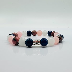 May include: A beaded bracelet featuring a variety of colorful gemstones. The bracelet includes pink, white, navy blue, and brown beads. A silver clasp secures the bracelet. The bracelet is displayed on a white surface.