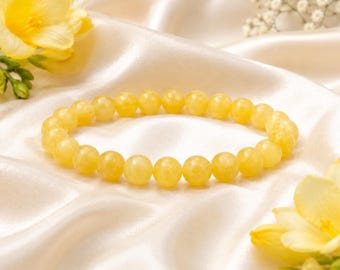 May include: A circular bracelet composed of smooth, round, translucent yellow beads. The beads are uniform in size and strung together to form a continuous loop, displaying a consistent pale yellow hue throughout the entire piece of jewelry.