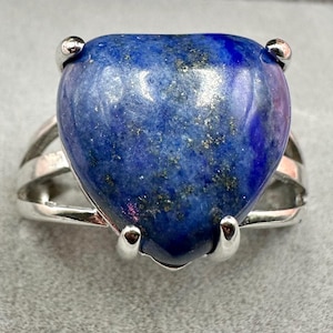 Puede incluir: Un anillo de plata con una gran piedra de lapislázuli en forma de corazón. La piedra es de un azul profundo con motas doradas.
