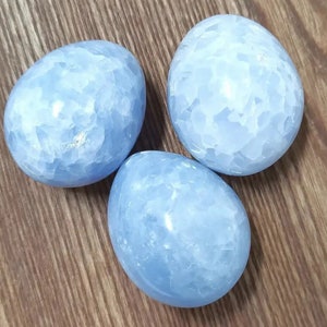 Può includere: Tre uova di cristallo di celestite blu. Le uova sono lisce e hanno un colore blu chiaro con vortici bianchi.