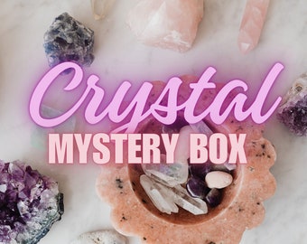 Op de afbeelding: Een roze en witte kristallen mystery box met een verscheidenheid aan kristallen, waaronder amethist, rozenkwarts en helder kwarts. De doos staat op een wit marmeren oppervlak.