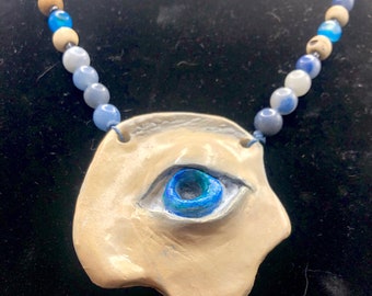 May include: A ceramic necklace with a blue eye pendant and a string of blue and white beads.