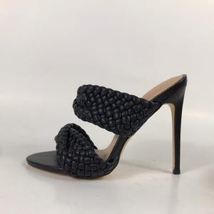 May include: Black high-heeled sandals with a woven design on the straps. The open-toe shoes have a stiletto heel and a smooth, solid sole. The sandals are set against a plain white background.
