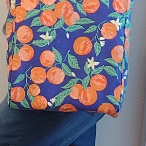 May include: A blue tote bag with a white handle and a pattern of orange citrus fruit and white flowers on a blue background.