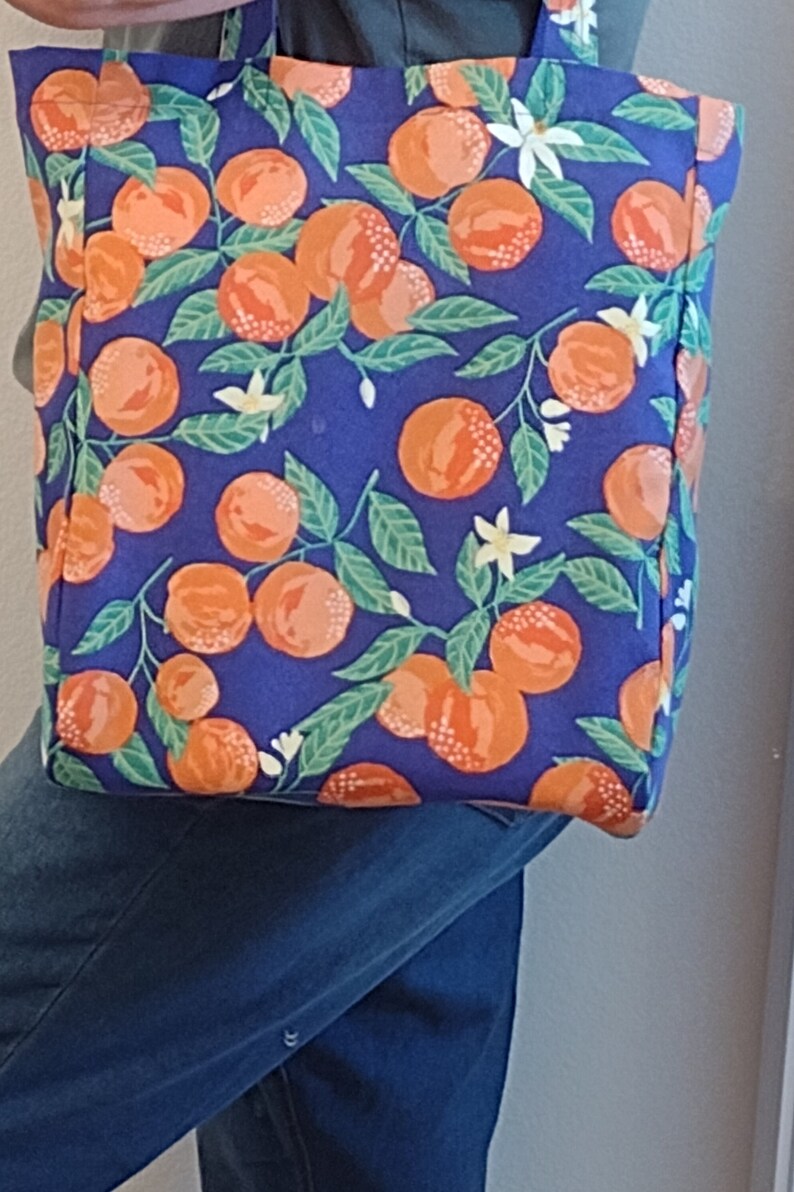 May include: A blue tote bag with a white handle and a pattern of orange citrus fruit and white flowers on a blue background.