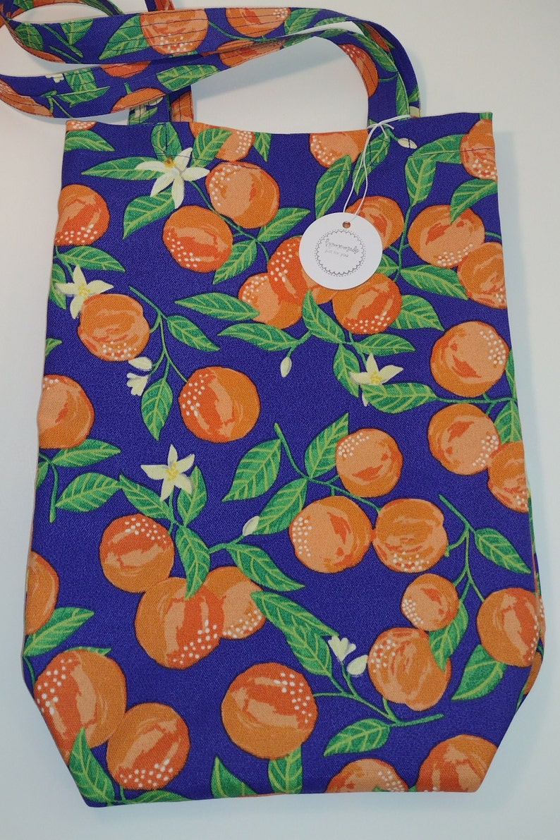 May include: A purple tote bag with a white strap and a white tag that says "Handmade just for you". The bag is decorated with a repeating pattern of orange citrus fruit and green leaves on a purple background.