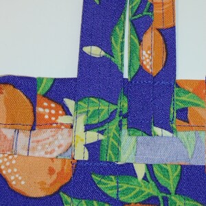 May include: A purple fabric tote bag with orange and green citrus fruit print. The bag has two straps.