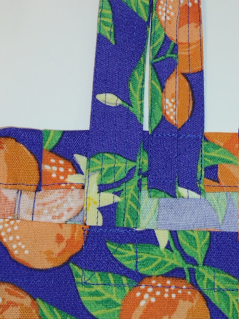 May include: A purple fabric tote bag with orange and green citrus fruit print. The bag has two straps.