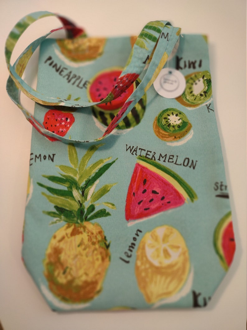 Peut inclure: Un sac cabas bleu clair avec une bandouli&egrave;re blanche. Le sac est imprim&eacute; d'un motif de fruits avec de la past&egrave;que, de l'ananas, du kiwi, du citron et des fraises. Les mots "Watermelon", "Pineapple", "Kiwi", "Lemon" et "Strawberry" sont imprim&eacute;s sur le sac.