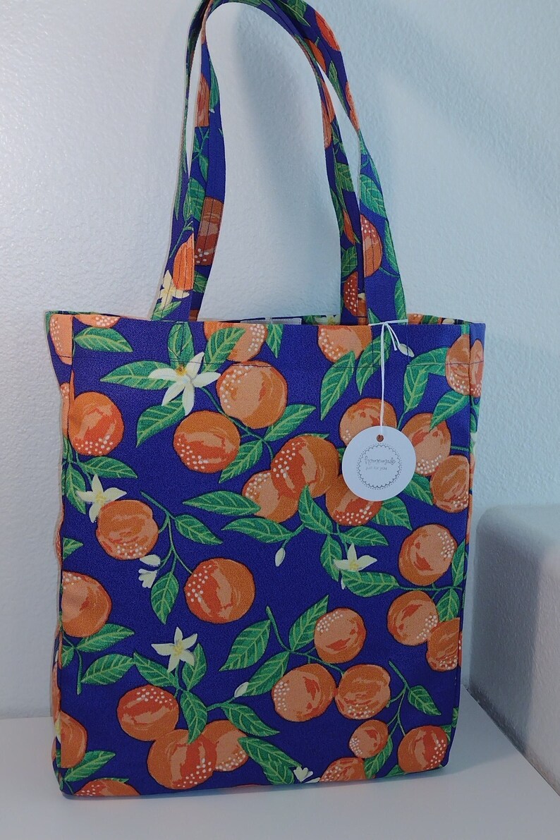 May include: A blue tote bag with a white tag that says "Remarkable" and a pattern of orange citrus fruit and green leaves.