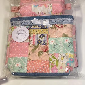 May include: A patchwork fabric bag and matching pencil case set. The bag features a denim blue border, white lace trim, and a white bow. The patchwork design includes pink, white, and floral patterns. The pencil case is pink with a floral pattern.
