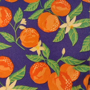 May include: Purple fabric with a repeating pattern of orange citrus fruit and white flowers. The fruit and flowers are on green stems and leaves.