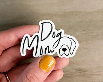 May include: White sticker with black text that reads "Dog Mom" with a simple black and white outline of a dog's head.