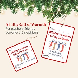 Two printable Christmas cozy sock gift tags displayed beneath evergreen branches and Christmas lights. The tags offer a thoughtful finishing touch for holiday sock gifts for teachers, friends, neighbors, and coworkers.