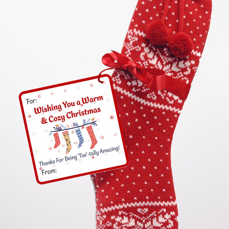 Close-up of a printable Christmas gift tag attached with red ribbon to cozy red patterned socks. The tag says “Wishing You a Warm & Cozy Christmas” and “Thanks for Being 'Toe'-tally Amazing!” with spaces for handwritten names.