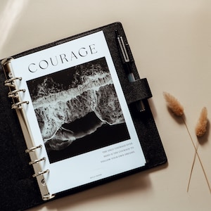 May include: A black and white photograph of ocean waves crashing on a beach. The photo is in a white planner with a black cover and silver rings. The planner has the word "COURAGE" printed on the front and the text "The only courage ever need is the courage to follow your own dreams." printed below the photo. The text "WILA PAPER" is printed in the bottom right corner.