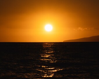 Pode incluir: Um pôr do sol laranja brilhante sobre um oceano azul escuro. O sol se põe à distância, lançando um brilho dourado sobre a água.