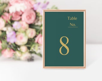 Könnte beinhalten: Eine goldene Tischnummernkarte mit der Nummer 8 auf dunkelgrünem Hintergrund. Die Karte ist in einem roségoldenen Rahmen und trägt die Aufschrift "Table No."